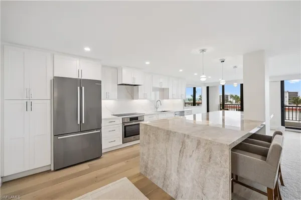 a kitchen with stainless steel appliances granite countertop a refrigerator a stove a sink a dining table and chairs with wooden floor