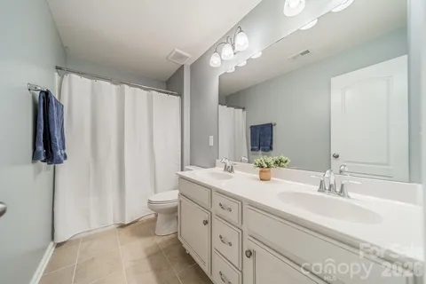 a spacious bathroom with a double vanity sink a toilet a mirror and shower curtain