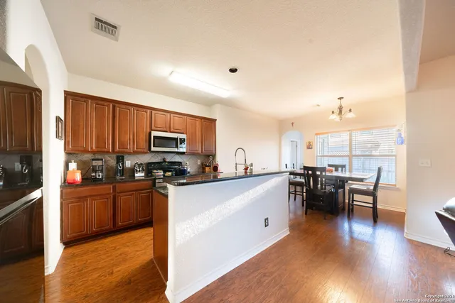 a kitchen with stainless steel appliances granite countertop a stove top oven a sink dishwasher a dining table and chairs with wooden floor