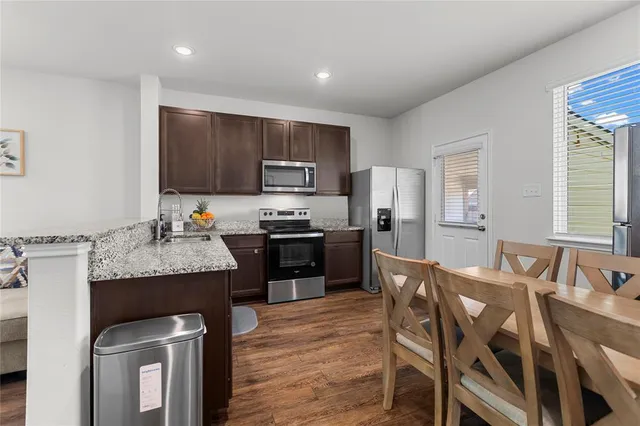 a kitchen with kitchen island granite countertop wooden cabinets a refrigerator a stove a oven with a dining table and chairs