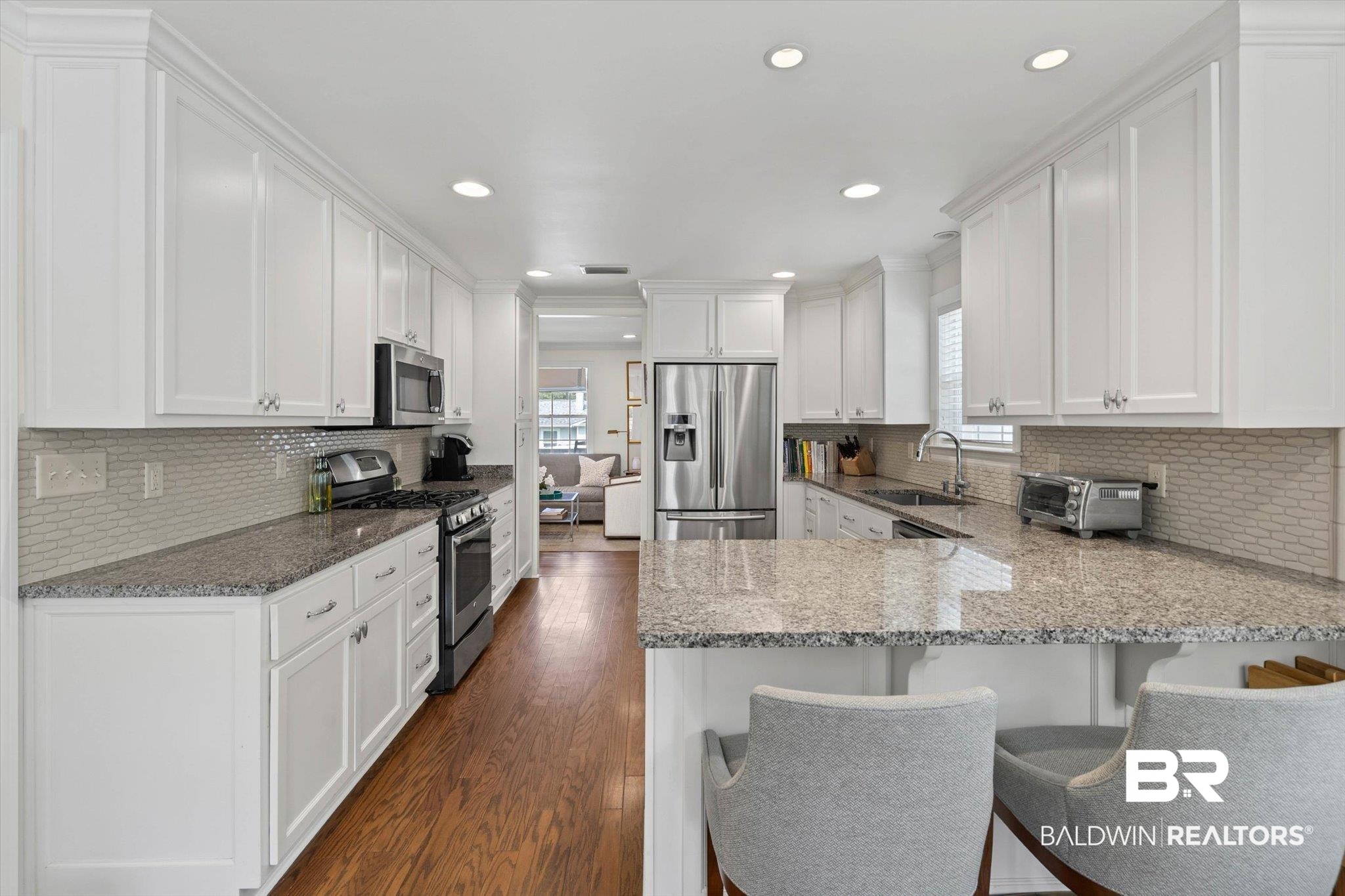 77 North Hathaway Road Mobile, AL 36608 - Photo 9 of 33 Kitchen featuring white cabinets, a peninsula, light stone countertops, appliances with stainless steel finishes, and decorative backsplash