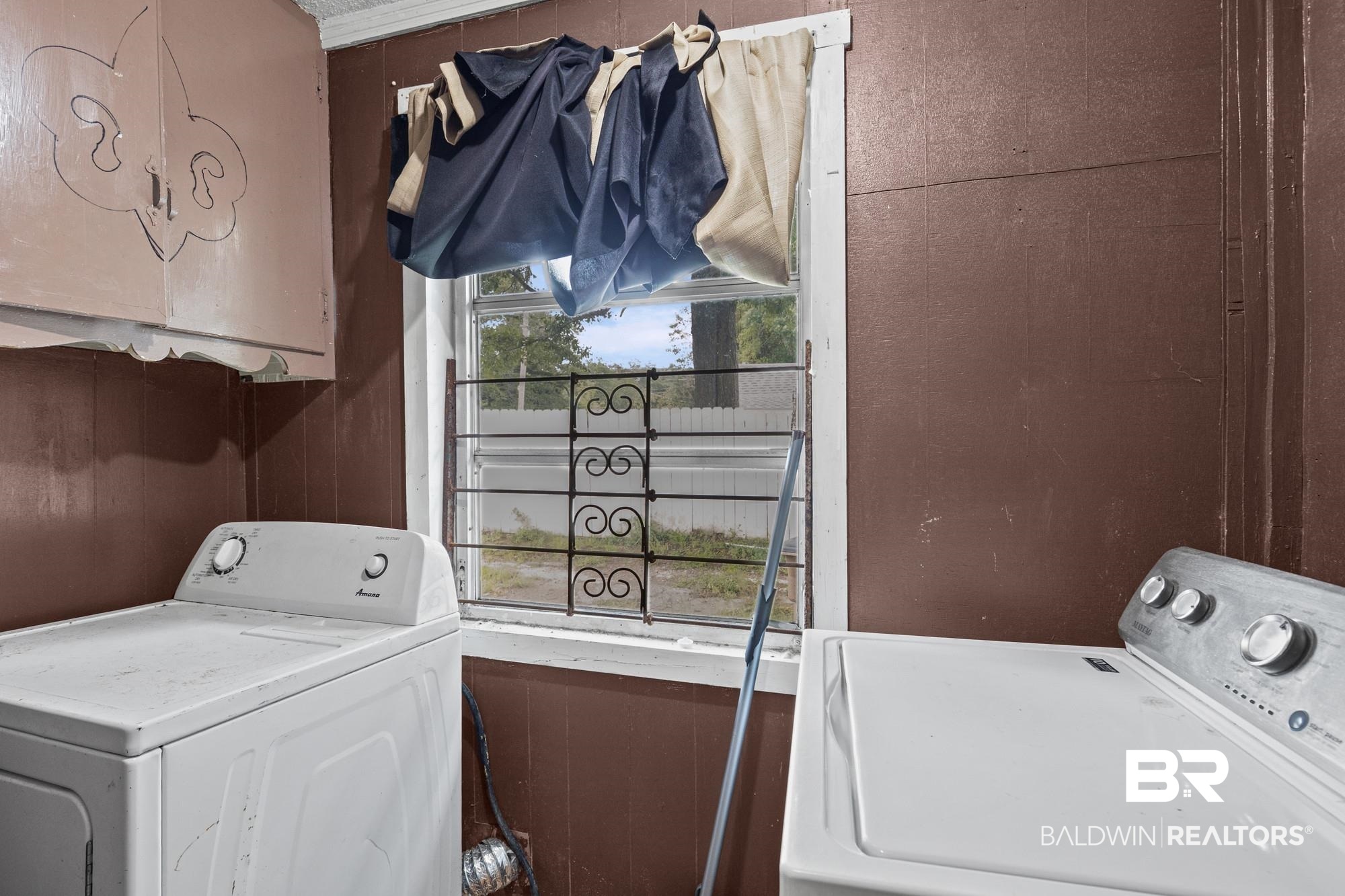 160 Glenn Avenue Mobile, AL 36606 - Photo 12 of 15 Room featuring a window with a decorative metal security grille, wood-finish wall paneling, and an overhead storage cabinet