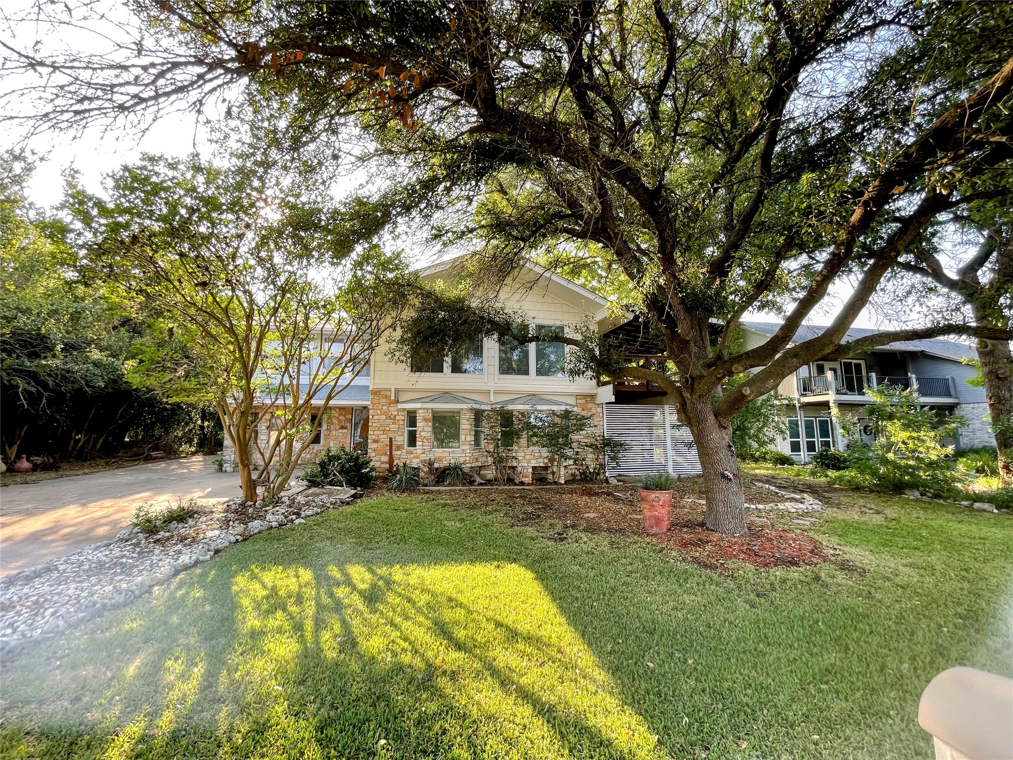 View of front of home featuring a balcony, a front yard, stone siding, and driveway