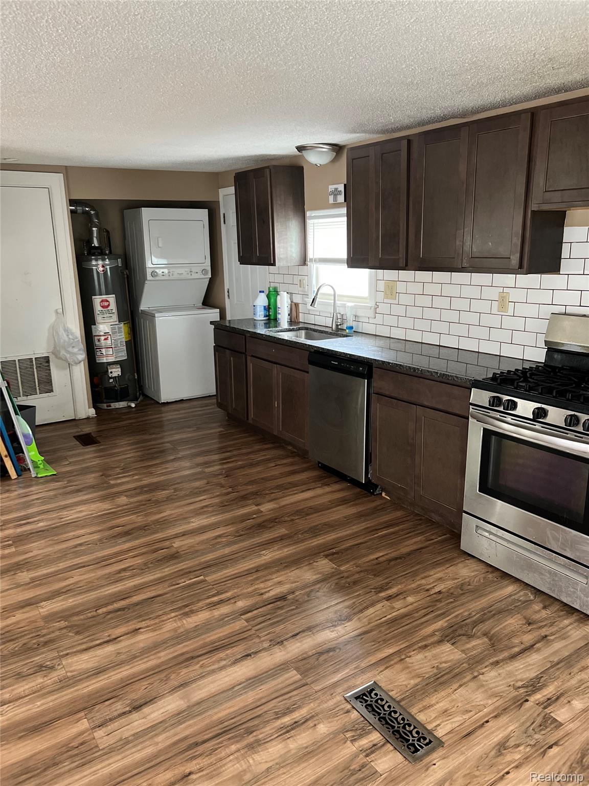 35945 Herman Street Romulus, MI 48174 - Photo 7 of 26 Kitchen with dark brown cabinetry, appliances with stainless steel finishes, stacked washing machine and dryer, dark wood-style flooring, and a textured ceiling