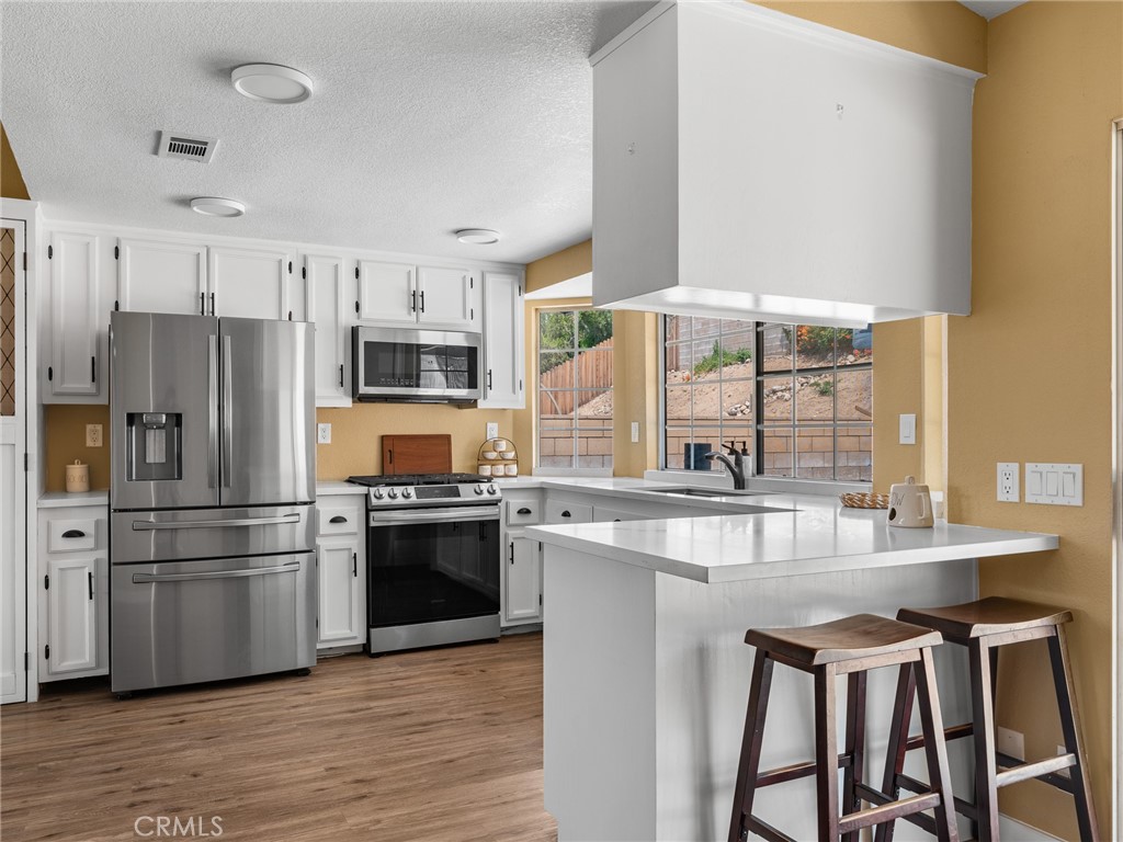 13901 Hidden Valley Road Victorville, CA 92395 - Photo 14 of 31 a kitchen with stainless steel appliances a refrigerator a stove a sink and white cabinets with wooden floor