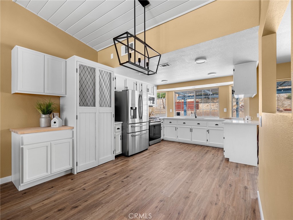 13901 Hidden Valley Road Victorville, CA 92395 - Photo 10 of 31 a kitchen with stainless steel appliances kitchen island a refrigerator a stove a sink dishwasher and white cabinets with wooden floor