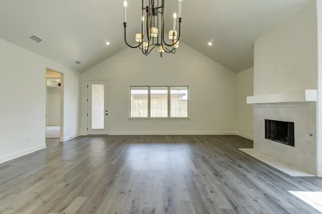 a view of an empty room with wooden floor fireplace and a window