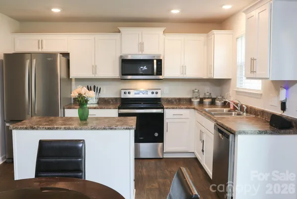 a kitchen with stainless steel appliances granite countertop a stove top oven a refrigerator a sink and dishwasher with white cabinets
