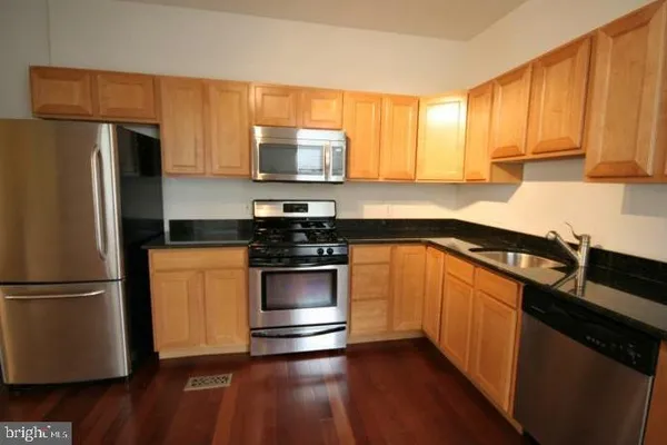 a kitchen with stainless steel appliances granite countertop a refrigerator a sink dishwasher a stove and white countertops with wooden floor