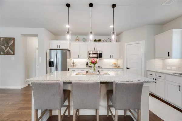 a kitchen with stainless steel appliances kitchen island granite countertop a dining table chairs and white cabinets