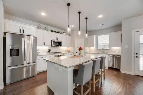 a kitchen with stainless steel appliances a stove a sink a refrigerator and chairs