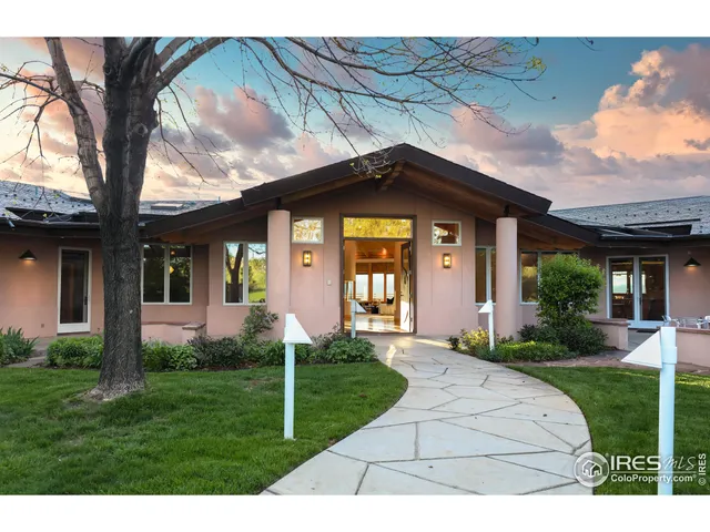 a view of a brick house with a large windows and a yard with plants and large trees