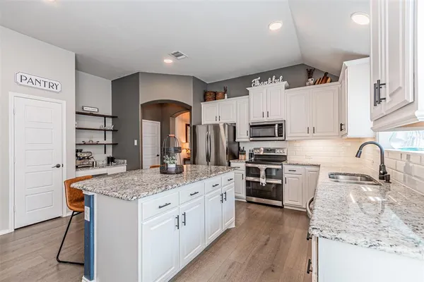 a kitchen with stainless steel appliances granite countertop a stove top oven a sink dishwasher and wooden cabinets with wooden floor