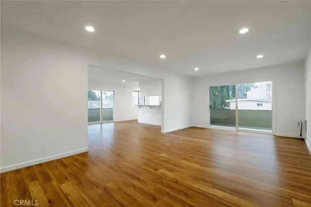a view of an empty room with wooden floor and a kitchen