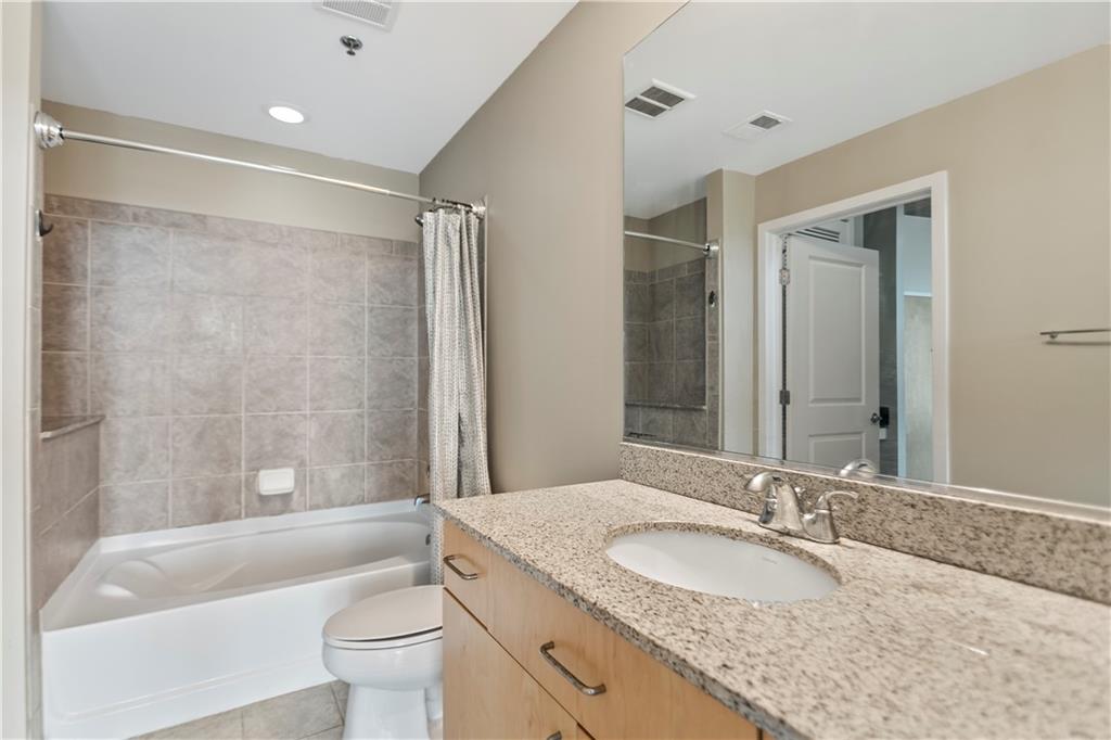 361 17th Street Northwest, Unit 1906 Atlanta, GA 30363 - Photo 13 of 28 a bathroom with a granite countertop sink a toilet a mirror a bathtub and shower