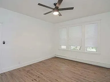 an empty room with wooden floor fan and windows