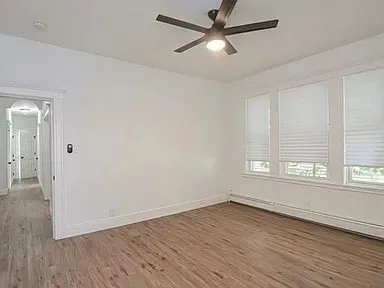 an empty room with wooden floor fan and windows