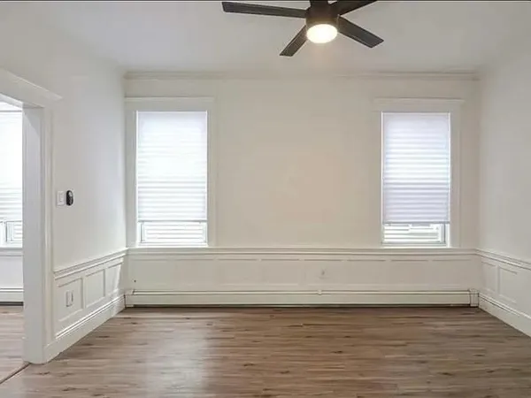 an empty room with wooden floor fan and windows