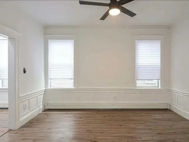 an empty room with wooden floor fan and windows