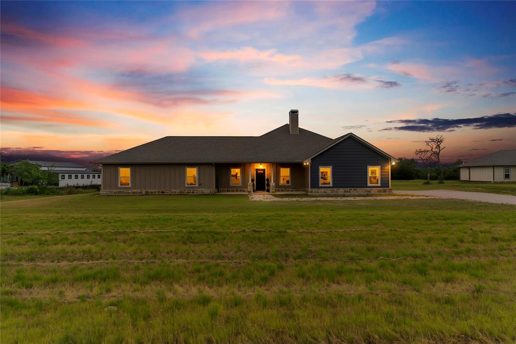 139 Kriston Lane Springtown, TX 76082 - Photo 2 of 39 Single-story residence featuring a dark asphalt shingle roof, stone accenting, dark blue siding, and tan vertical siding