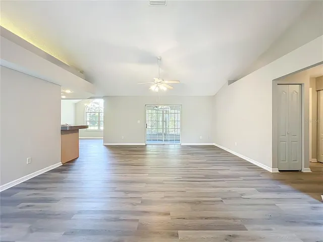 an empty room with wooden floor fan and windows