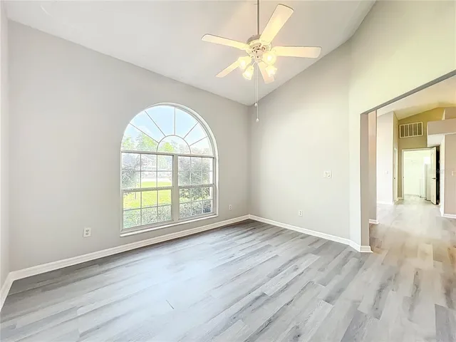 an empty room with wooden floor chandelier fan and windows