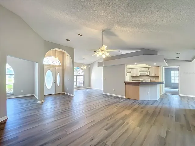 an empty room with wooden floor chandelier fan and windows