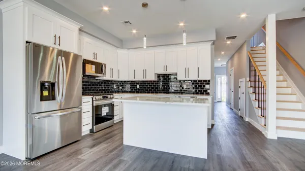a kitchen with stainless steel appliances granite countertop a refrigerator a stove a sink and white cabinets with wooden floor