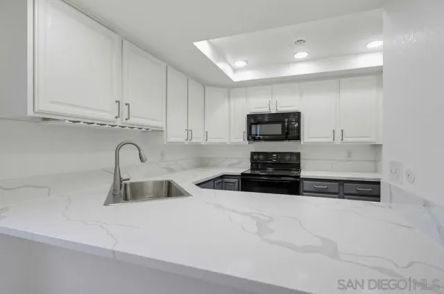 a kitchen with granite countertop a sink and a stove top oven with white cabinets