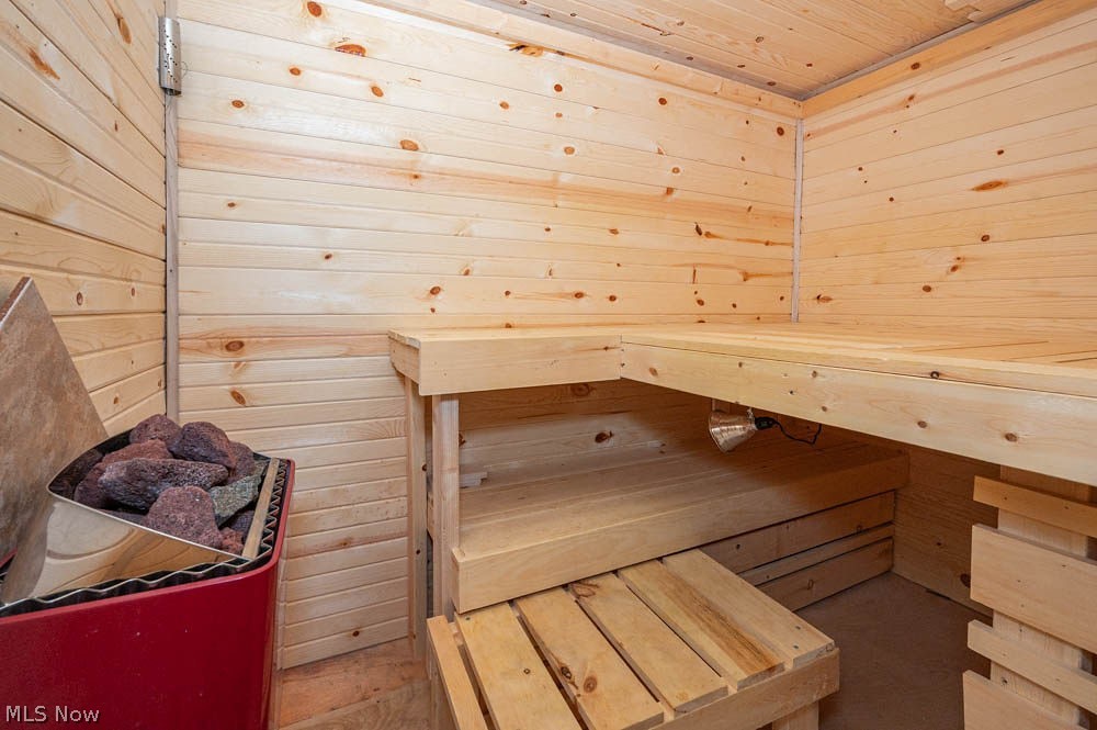 6787 South Palmyra Road Canfield, OH 44406 - Photo 20 of 30 Wood-paneled sauna featuring tiered wooden benches, slatted wood flooring, and a red sauna heater with stones