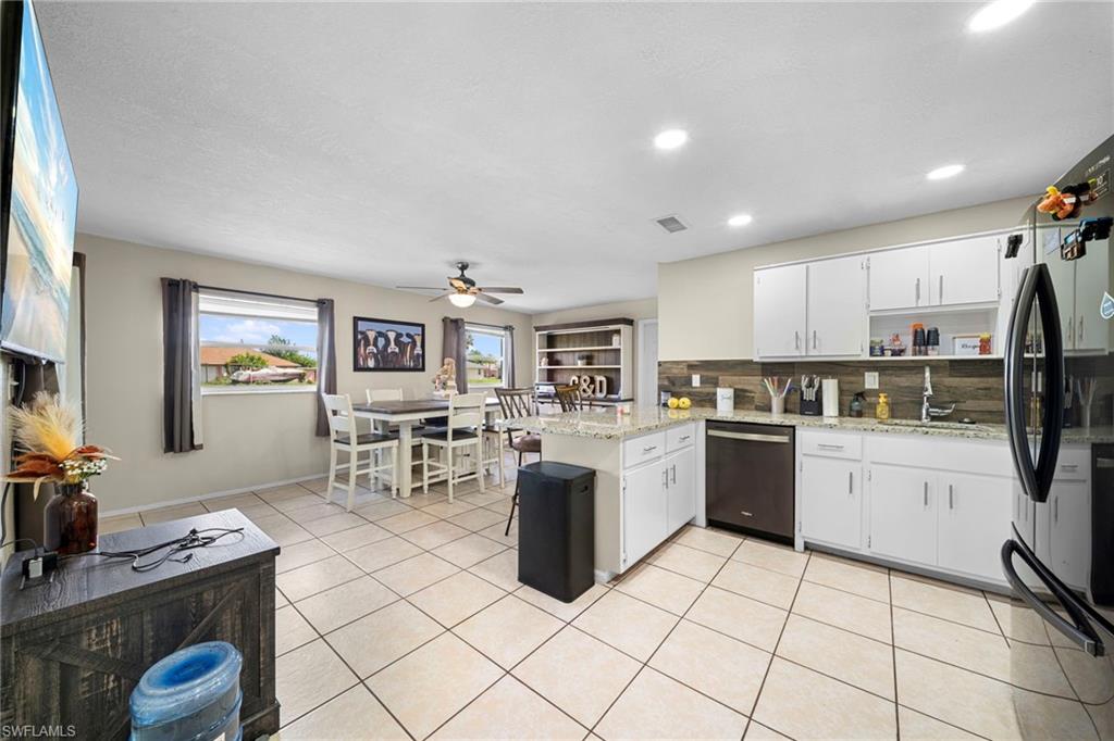 7289 Barragan Road Fort Myers, FL 33967 - Photo 4 of 18 Open-concept kitchen and dining area featuring white cabinetry, light-toned granite-style countertops, and a wood-finish backsplash