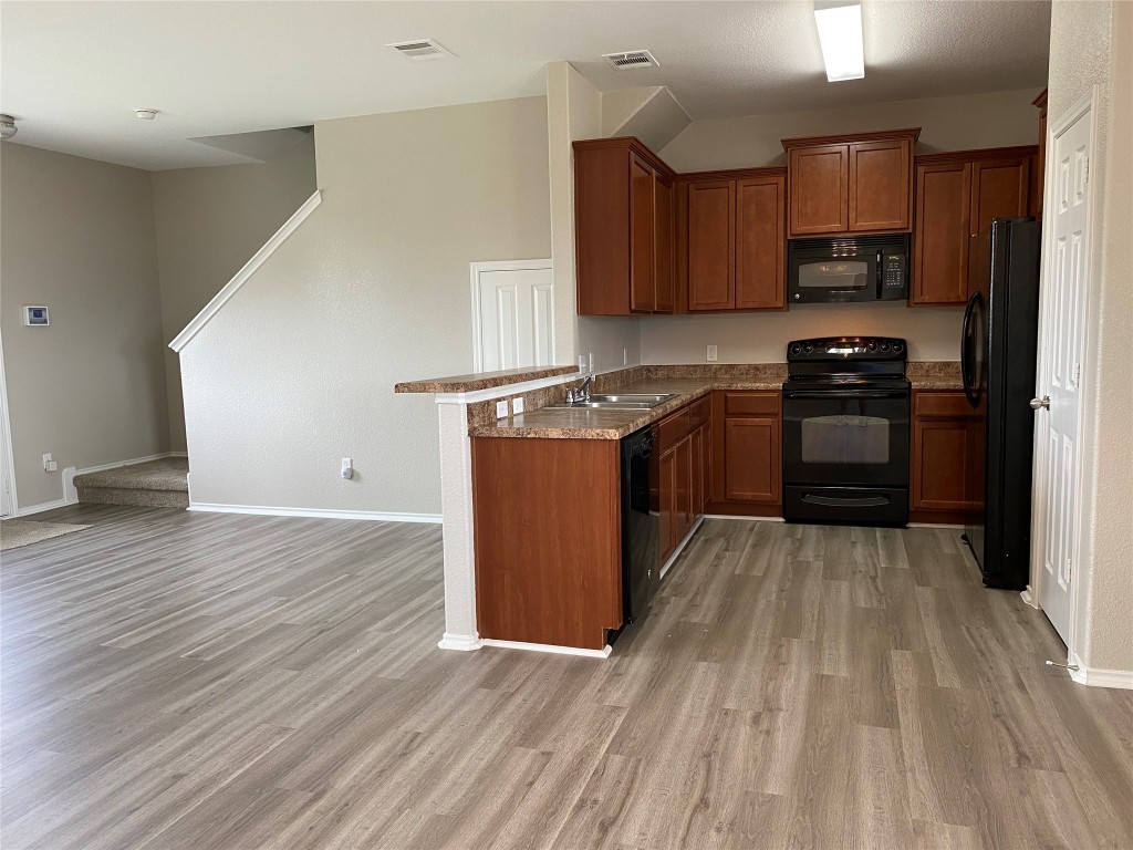 304 Azurite Drive Jarrell, TX 76537 - Photo 10 of 24 Kitchen featuring black appliances, a peninsula, brown cabinets, and light wood-style floors