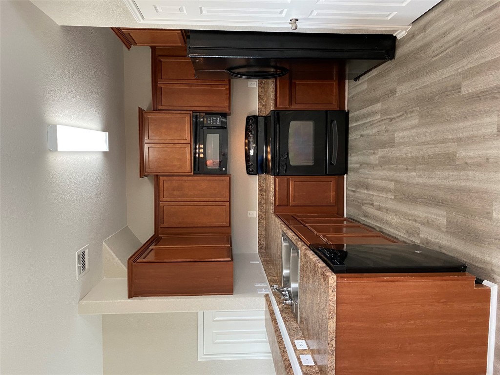 304 Azurite Drive Jarrell, TX 76537 - Photo 12 of 24 Kitchen featuring black appliances, light wood finished floors, brown cabinets, a peninsula, and dark countertops