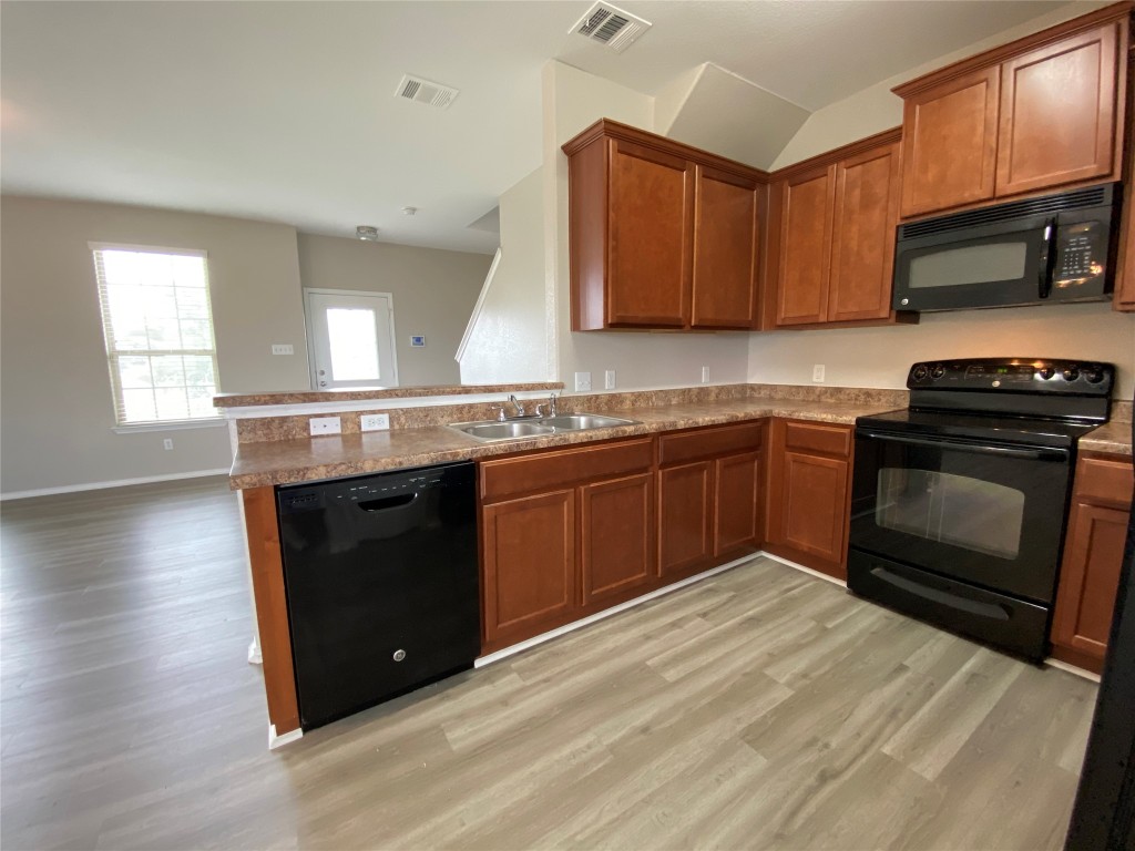 304 Azurite Drive Jarrell, TX 76537 - Photo 22 of 24 Kitchen featuring black appliances, light wood-style floors, brown cabinets, a peninsula, and vaulted ceiling