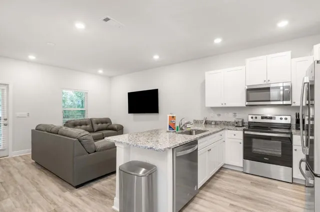 a living room with stainless steel appliances kitchen island granite countertop a sink and a stove top oven with wooden floor