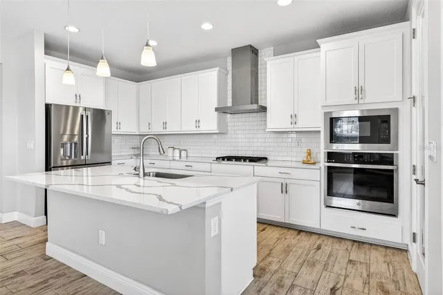 a kitchen with stainless steel appliances granite countertop a sink stove a refrigerator and white cabinets with wooden floor