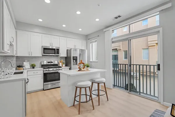 a kitchen with stainless steel appliances granite countertop a stove top oven a sink a refrigerator with white cabinets and wooden floor