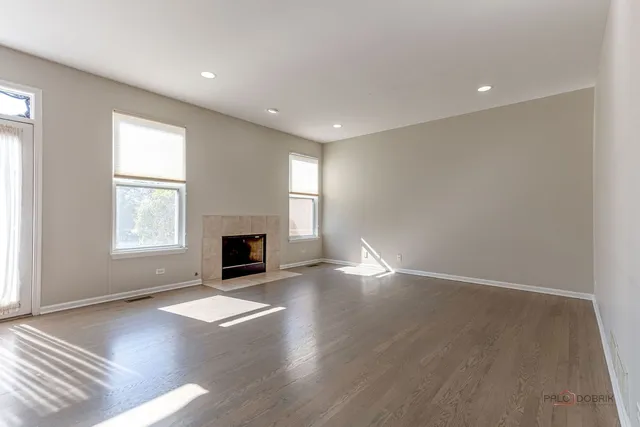 an empty room with wooden floor fireplace and windows