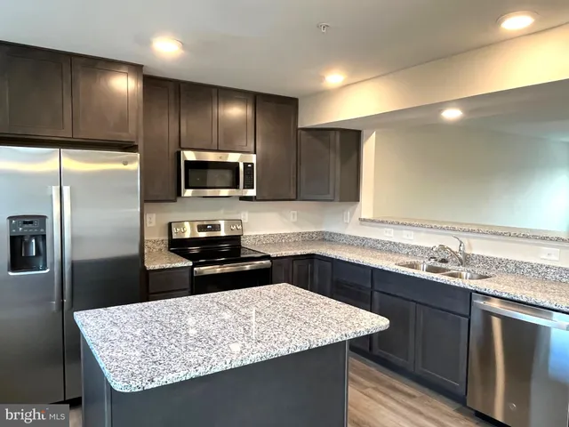 a kitchen with granite countertop kitchen island stainless steel appliances a sink stove refrigerator and a counter top