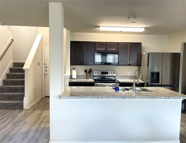 a kitchen with stainless steel appliances a sink a stove a microwave a refrigerator a cabinets and wooden floor