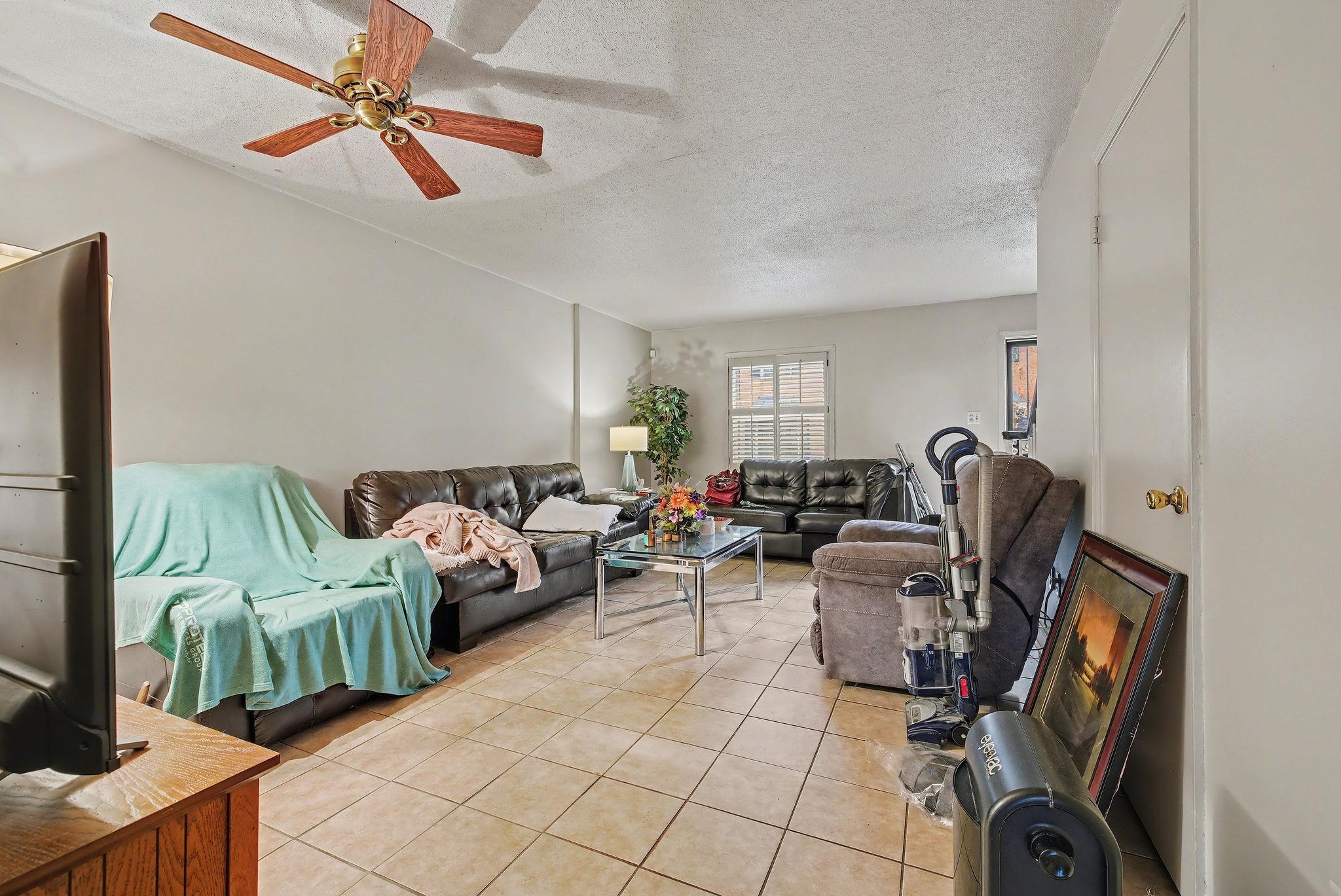 Living room with a textured ceiling, light tile patterned floors, and ceiling fan