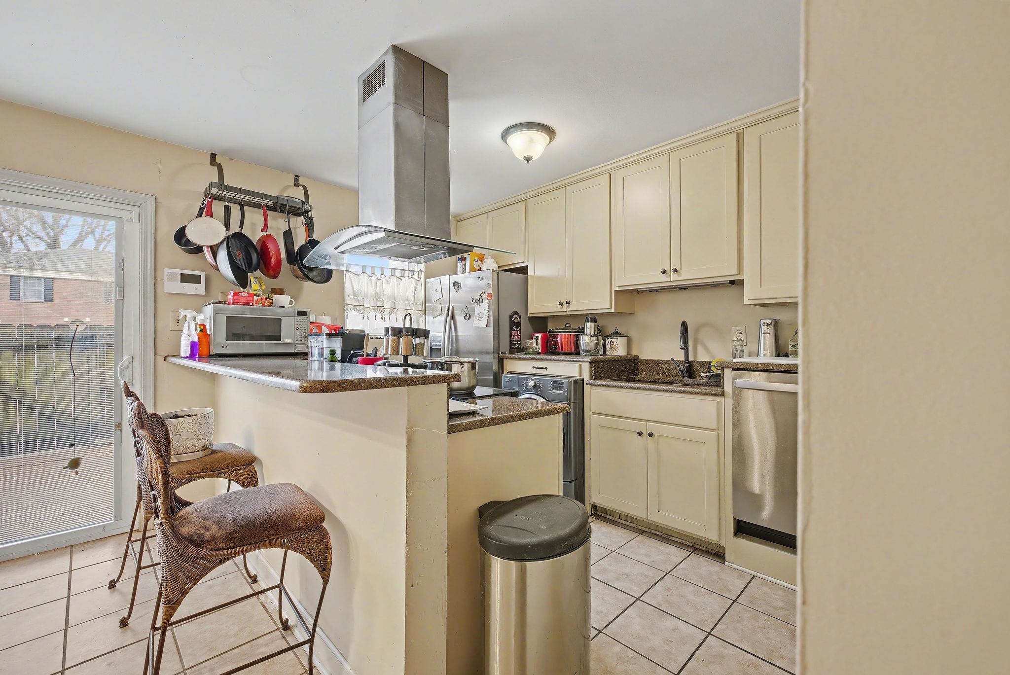 Kitchen featuring cream cabinetry, a breakfast bar, island exhaust hood, dark stone counters, and a peninsula