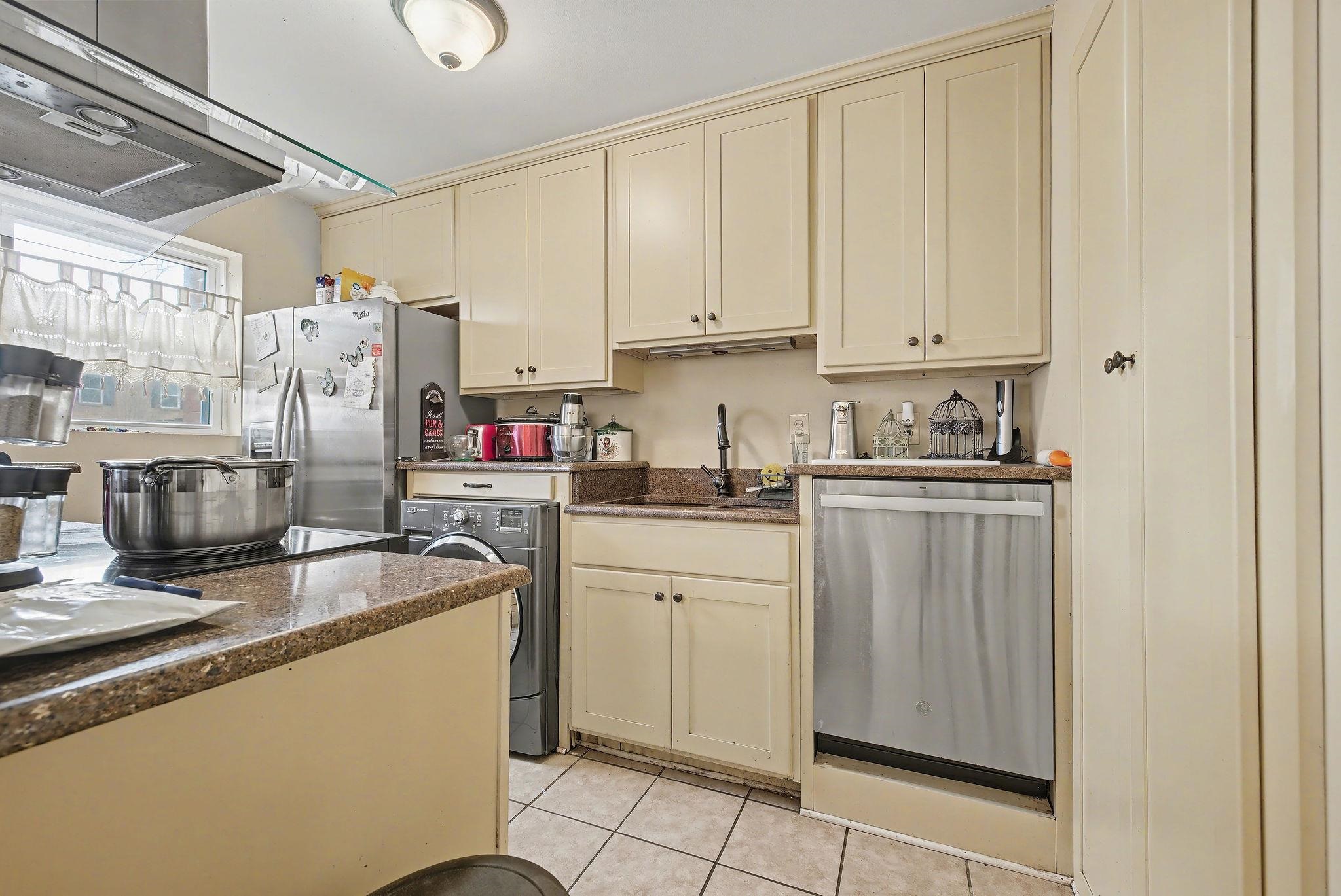 Kitchen with cream cabinets, ventilation hood, stainless steel appliances, dark stone countertops, and washer / clothes dryer
