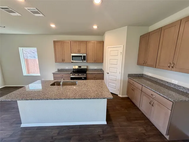 a kitchen with kitchen island granite countertop a stove top oven a sink a counter top space and cabinets