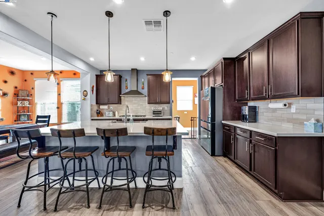 a kitchen with stainless steel appliances kitchen island granite countertop a stove a sink a oven a dining table and chairs with wooden floor