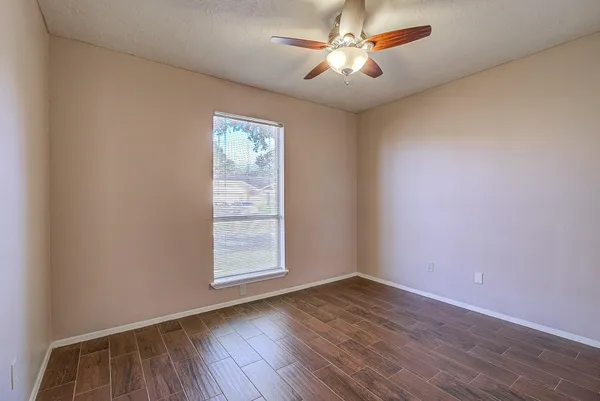 an empty room with wooden floor ceiling fan and windows