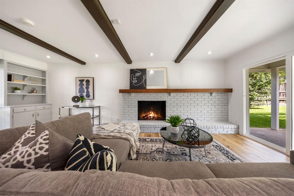 3060 Timberview Road Dallas, TX 75229 - Photo 13 of 39 Living area featuring exposed ceiling beams, built-in shelving, a white brick fireplace with a wood mantle, recessed lighting, and wood-finish flooring