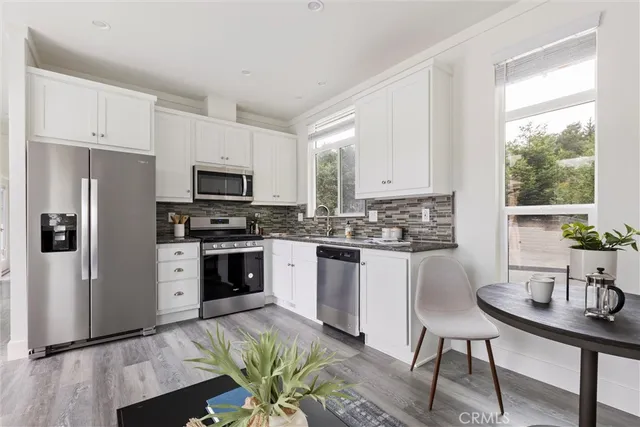 a kitchen with stainless steel appliances a stove a sink a microwave a refrigerator white cabinets and wooden floor