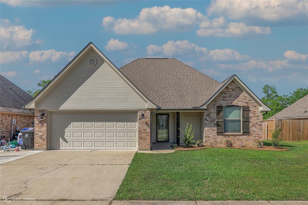 View of front of property with fence, a front lawn, brick siding, an attached garage, and driveway