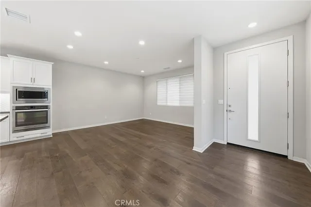 an empty room with wooden floor fridge and windows